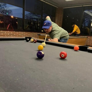 Student lines up a shot at a billiards table