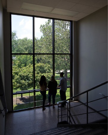 three students standing at hallway window