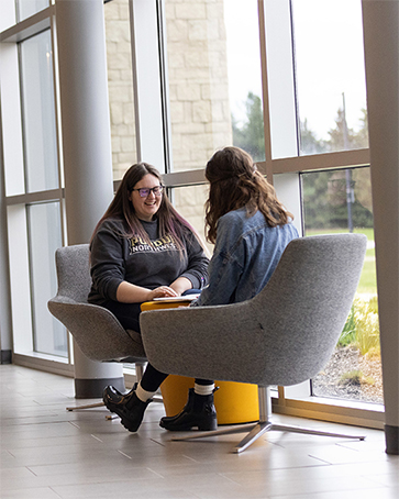 Two students sit across from each other and talk