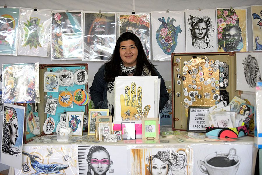 Artist stands in a booth surrounded by her artwork