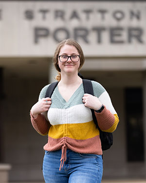 Student stands outside of Porter Hall. She is wearing a backpack and her hands are gripping the straps.