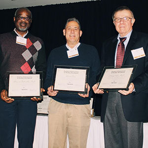 Three people stand together with awards