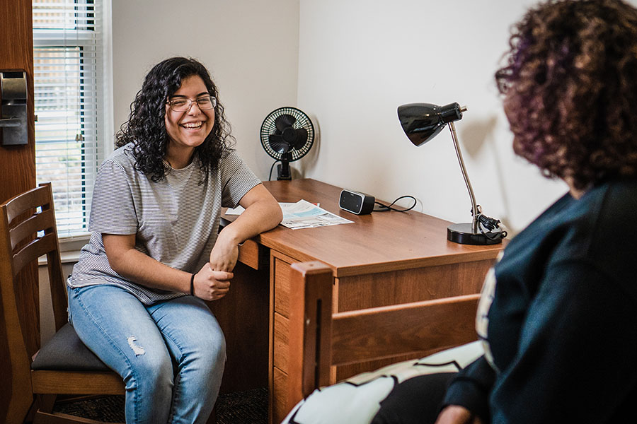 Two students sit and talk in a dorm room.