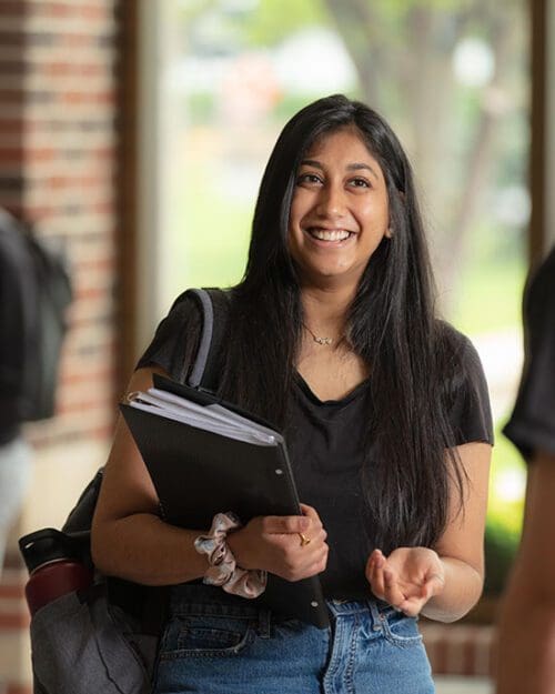 A student smiles while holding a folder.