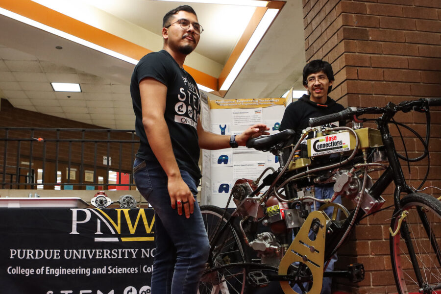 Jaime Sahagun, left, and Enoc Gutierrrez, third-year Mechatronics Engineering Technology majors, show off the Fluid Power Club bike during a “STEM on the Road” visit at East Chicago Central High School.