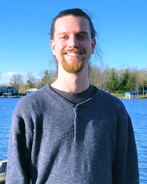 Fall 2022 PNW graduate Ryan Frederick stands in front of a lake.