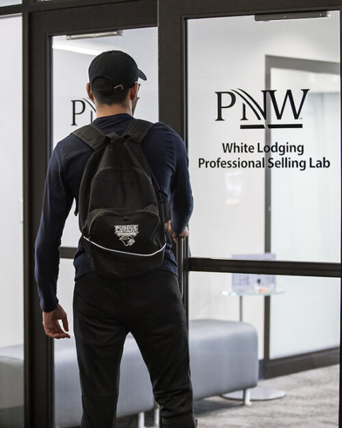 A student stands in front of a door for PNW's White Lodging Professional Selling Lab