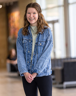 A student stands and smiles in a hallway