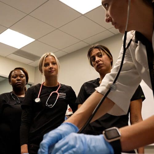 Three nursing students look at their instructor