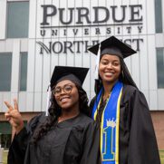 Two students pose in commencement regalia in front of the Nils Building