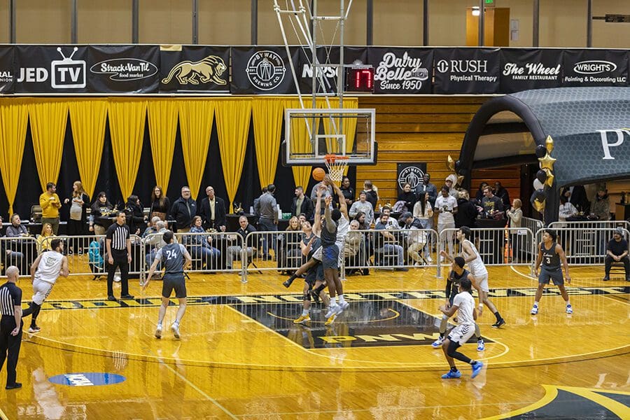 Men's basketball players jump for a ball underneath the net