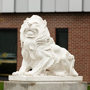 A lion statute with a brick wall and windows in the background
