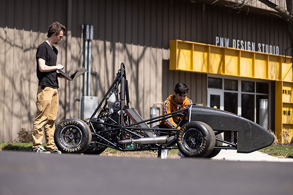 Two students work on a formula SAE car outside of the PNW Design Studio