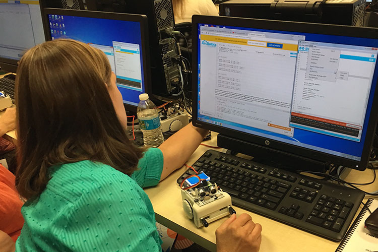 A woman works with a small robot at a computer