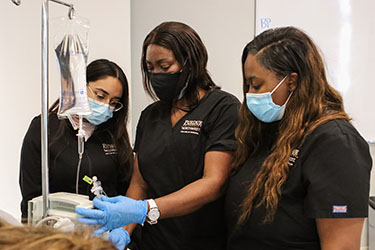 PNW nursing students in masks work with an IV pole