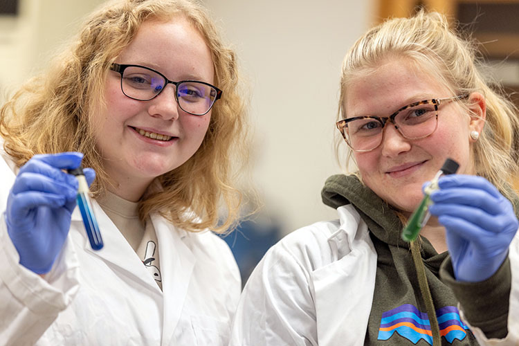 Students in lab coats hold test tubes