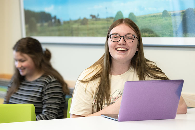 A student smiles at a computer.