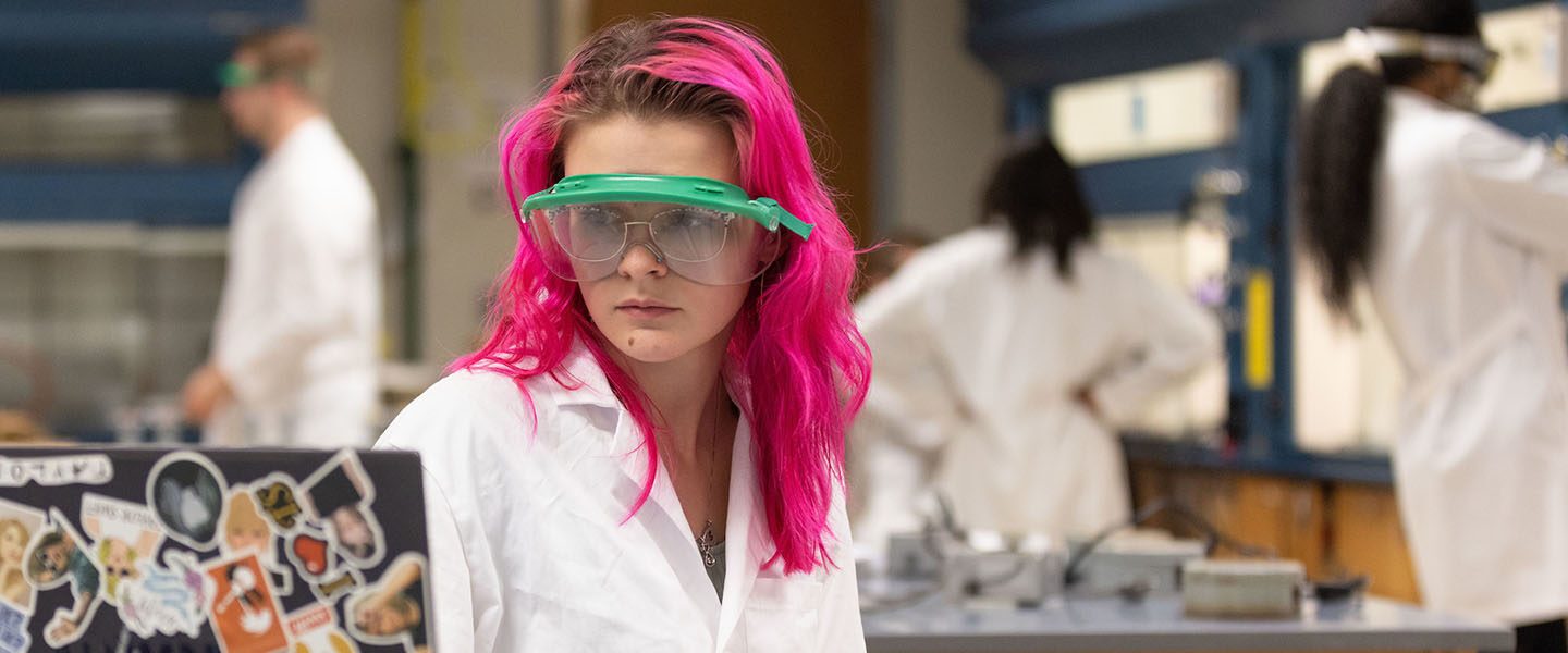 A biology student wearing PPE and a lab coat.