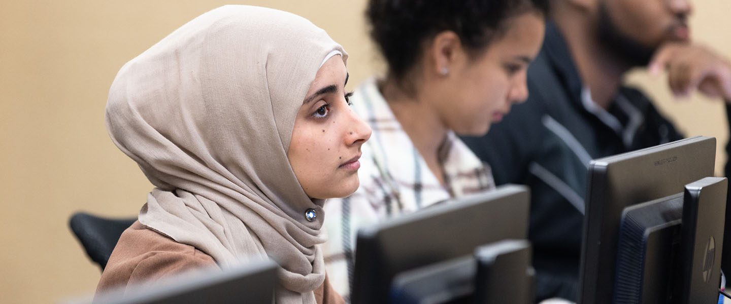 A student in a head scarf listens in a computer classroom