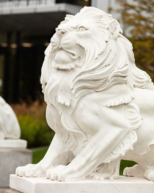 A lion statue with a building and greenery in the background