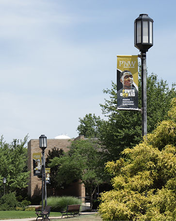 A PNW campus view with greenery, lampposts and banners.
