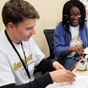 Students sit at a table and work on a wired device