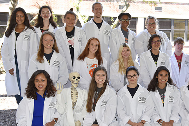 Participants in PNW's forensic science summer camp pose in lab coats with a skeleton (also in a lab coat)