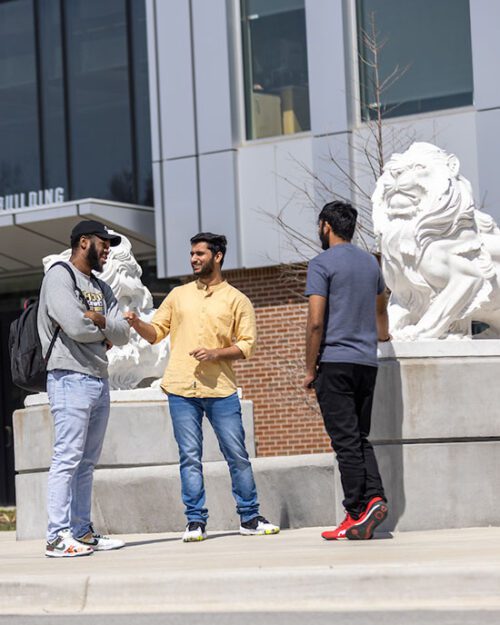 Three students stand outside, near lion statues