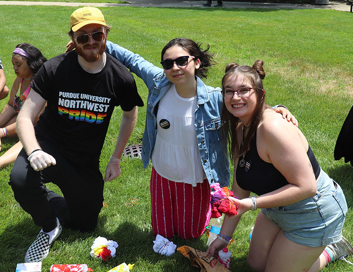 Three students pose together outdoors while tie dying shirts