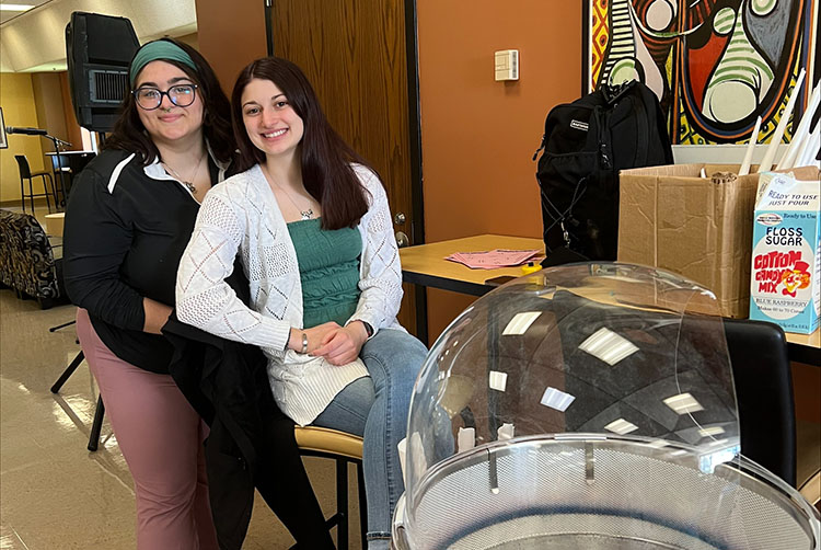 Two students pose next to a cotton candy machine