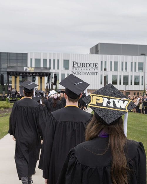 PNW graduates in the procession at spring 2023 commencement. A mortar board decorated with PNW is visible, as is the Nils K. Nelson Bioscience Innovation Building in the background.