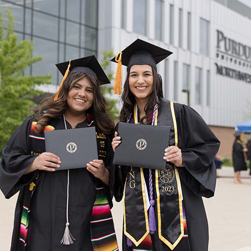 Two PNW graduates hold their diplomas in front of the Nils K. Nelson Bioscience Innovation Building at spring 2023 PNW commencement.