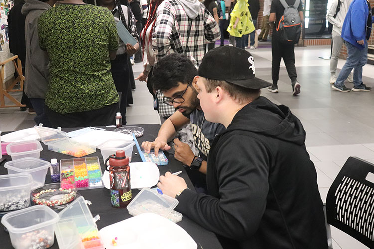 Students sit at a table covered with beads and glitter.