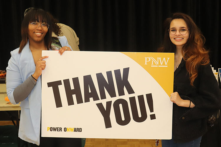 Two students stand together and hold a PNW branded "Thank You" sign