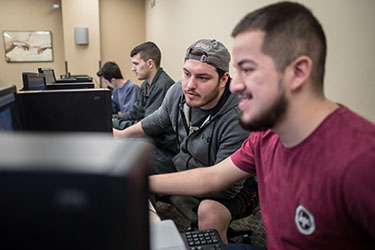 Students sit at a row of computers