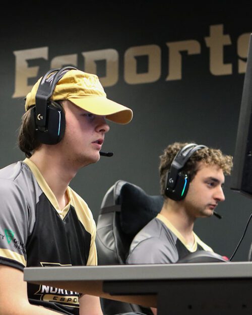 Two students sit in the PNW Esports arena. They are both wearing headsets.