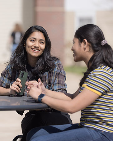 Two students sit at a table outside of University Village