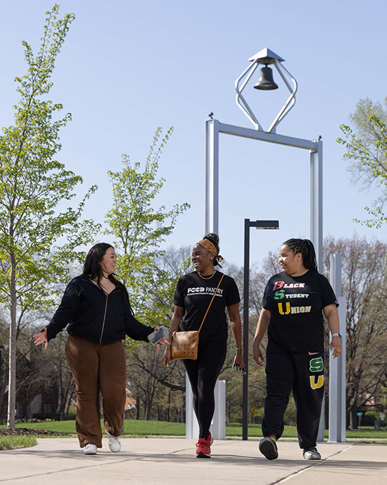 Three students walk outdoors on the Hammond Campus. The PNW Bell Tower is pictured behind them.