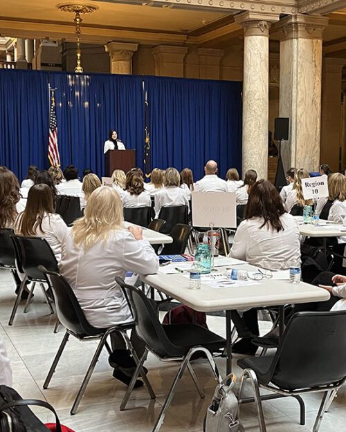 People in white nursing coats sit at white tables in the Indiana statehouse