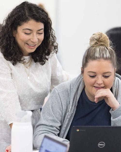 A student looks at a laptop. Their professor is standing behind them