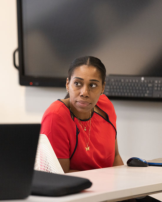 A student in a red shirt sits at a table. They are slightly leaning to the left