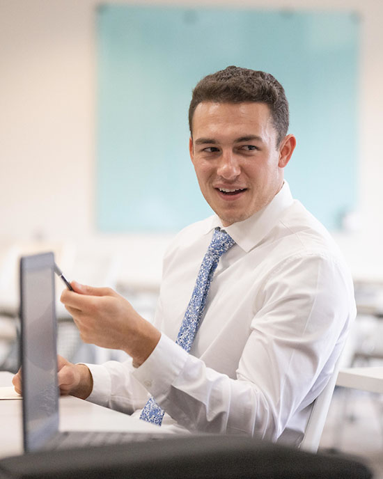 A student in a dress shirt and tie sits at a table