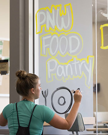 A student decorates a window to promote the PNW food pantry