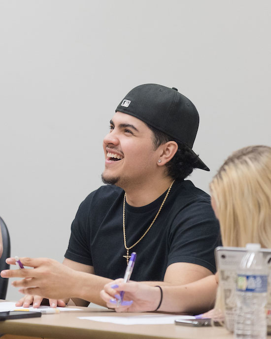 A student sits at a desk and smiles