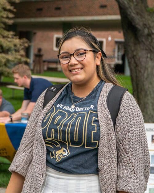 A student stands in a PNW Pride shirt and a beige cardigan