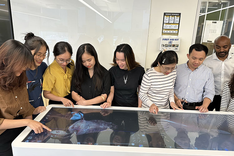 Eight people stand over a Anatomage table. They are all looking down