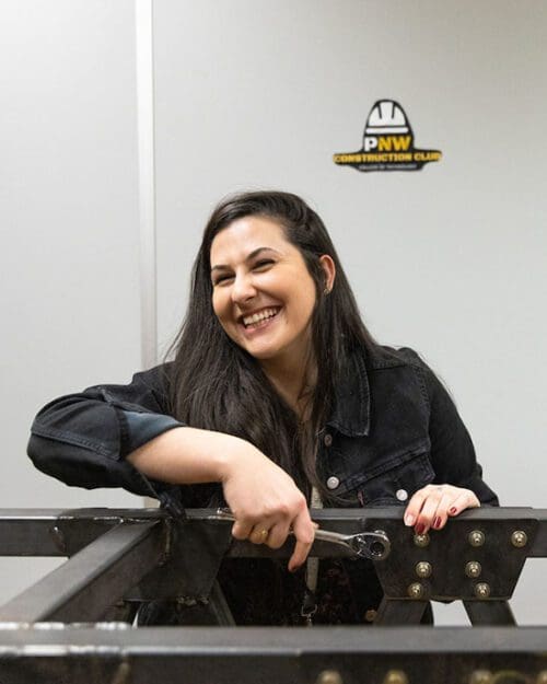 A student in a black denim jacket turns a wrench and smiles