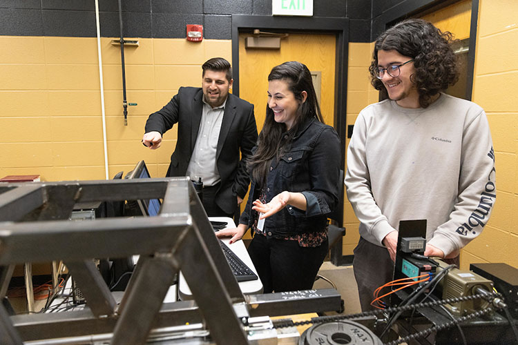 Two students stand with a professor during an engineering lab.