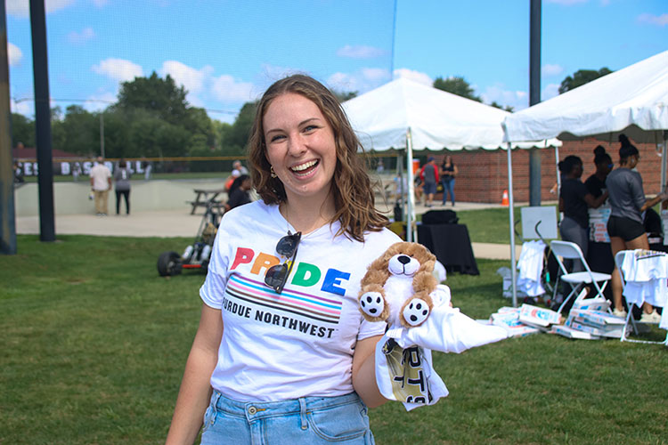 A PNW student wearing a "Pride" shirt smiles while holding up PNW merchandise.
