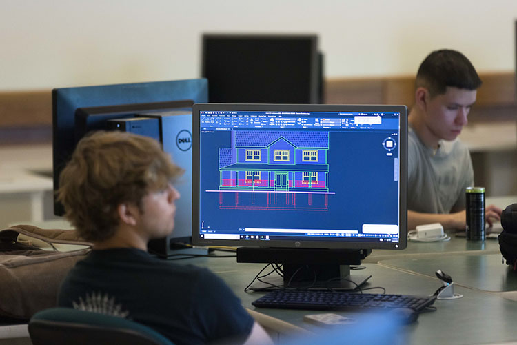 A student sits in class. There is a digital model of a house on the computer screen in front of them